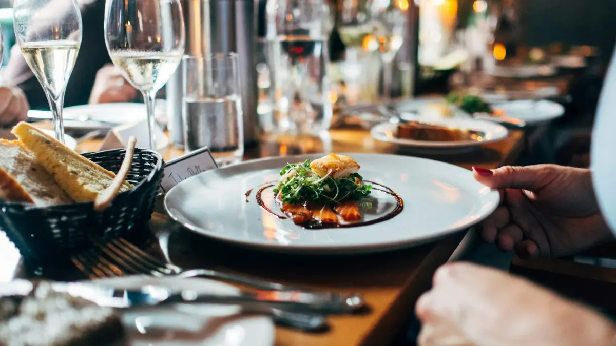 Service du soir dans un restaurant : une assiette dressée posée sur une table, entre les verres de vin blanc et la corbeille de pain