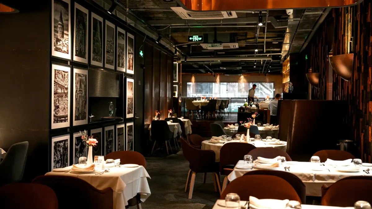 Salle de restaurant aux tables dressées, nappes blanches et verres prêts, avant l'arrivée des clients